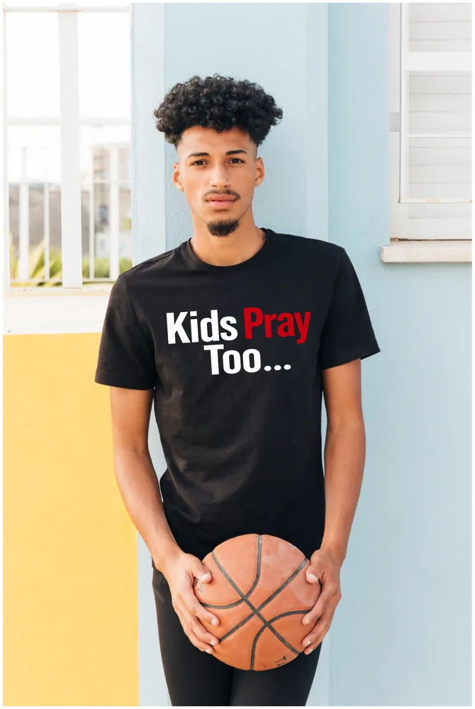 Teen holding a basketball in a black Kids Pray Too tee