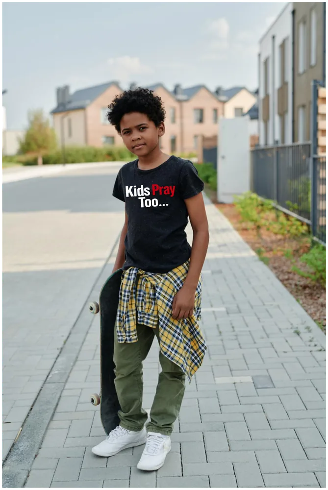 Teen with a skateboard wearing a black Kids Pray Too tee