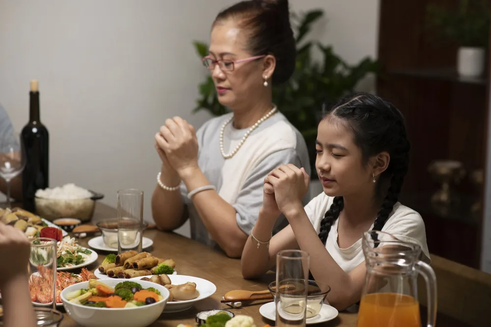 Family holding hands in prayer at the dinner table