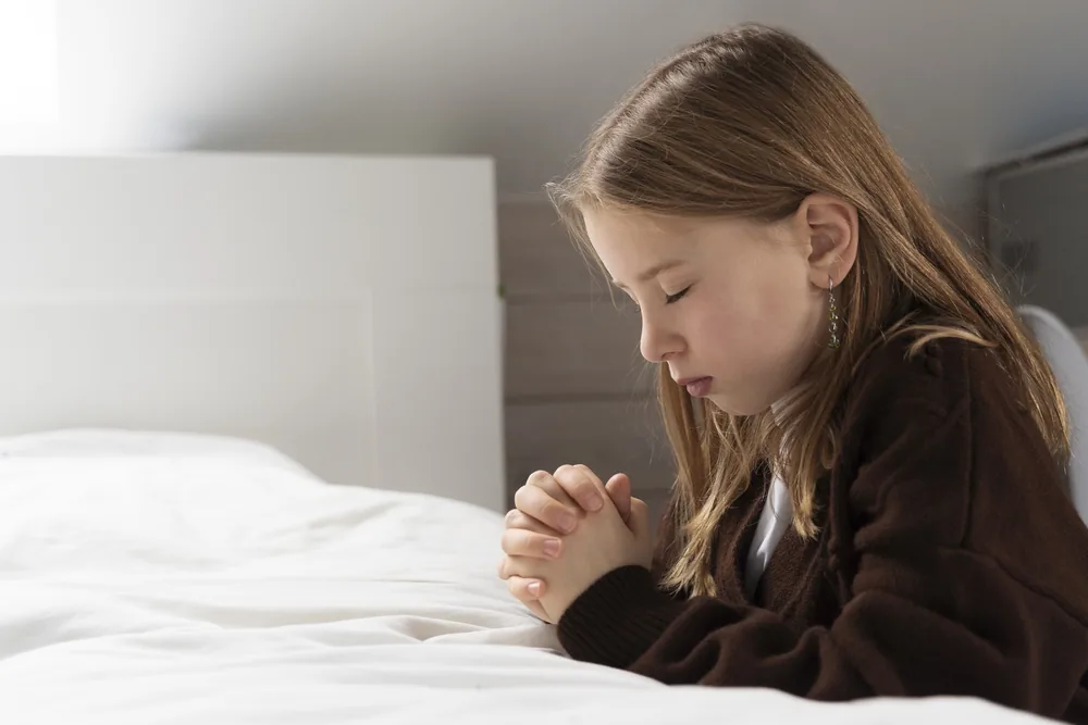 Child praying with folded hands at bedtime